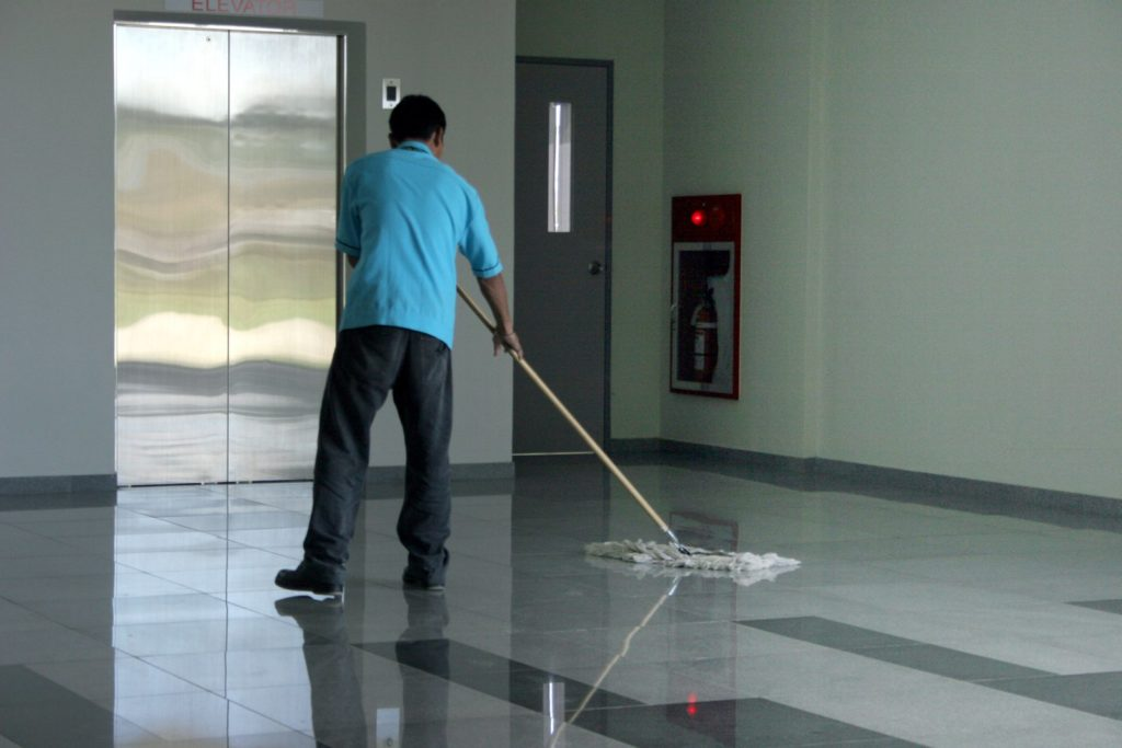 Profissional de limpeza conservando o hall de um edifício, ao lado do elevador